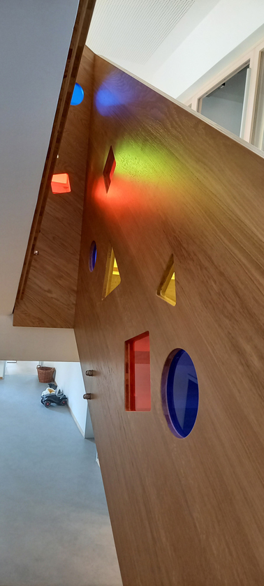 Treppenaufgang modern gestaltet; Geländer als Holzwand mkt farbig, gläsernen Aussparungen